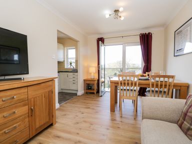 A dining area with a wooden table and chairs next to sliding glass doors with red curtains in a room with a wooden sideboard and a beige sofa at Claife Heights in Windermere