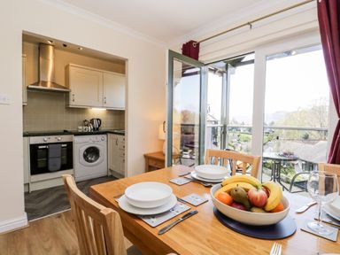 A dining table with plates and a fruit bowl near an open door leading to a kitchen and balcony at Claife Heights in Windermere