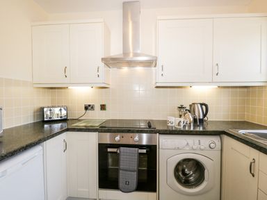 A kitchen with white cabinets a stove a washing machine a toaster and a kettle at Claife Heights in Windermere