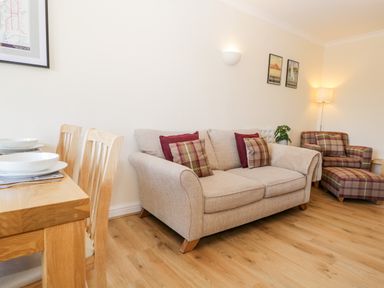 A living room with a beige sofa and plaid armchair with ottoman near a wooden dining table at Claife Heights in Windermere