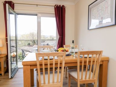 A dining area with a wooden table and chairs set with plates and glasses near a glass door and window with red curtains at Claife Heights in Windermere