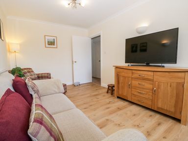 A living room with sofa and armchair a wooden TV cabinet and a wall-mounted television at Claife Heights Windermere