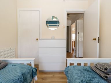 A bedroom with two beds covered in blue blankets and a white chest of drawers with a round mirror above it at Claife Heights in Windermere