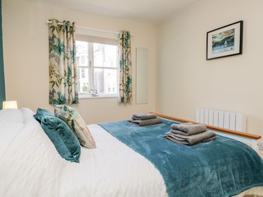 A bedroom with a bed with teal and floral pillows and a blue blanket with folded towels on top at Claife Heights in Windermere