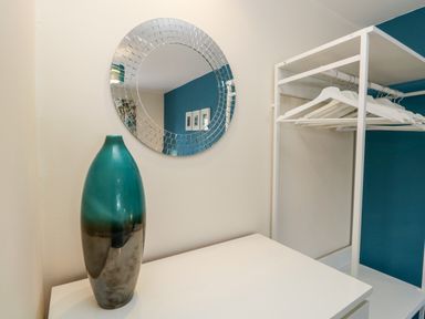 A teal and gray vase on a white surface with a round mirror and a white clothing rack with hangers in a room at Claife Heights in Windermere
