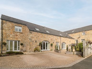 Exterior view of a stone building with multiple white doors and windows and potted plants at Calm Skies in Scremerston near Berwick-Upon-Tweed
