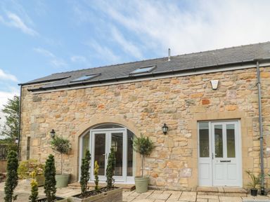 Exterior view of a stone building with arched glass doors a front door and potted plants at Calm Skies in Scremerston near Berwick-Upon-Tweed