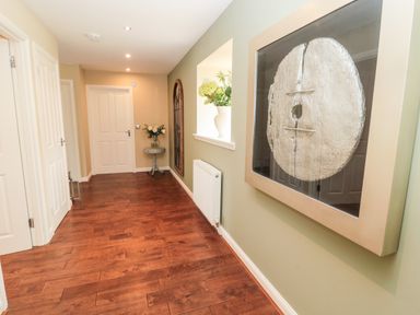A hallway with wooden flooring a framed artwork on the wall a small table with flowers and white doors at Calm Skies Scremerston near Berwick-Upon-Tweed