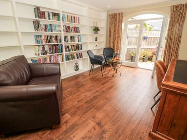 A room with wooden floor a leather sofa black chairs a round glass table bookshelves and doors leading outside at Calm Skies Scremerston near Berwick-Upon-Tweed