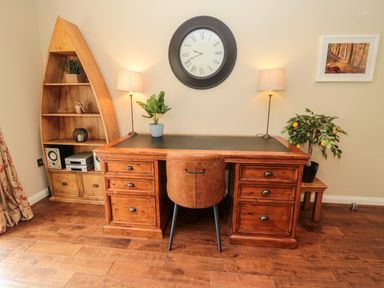 A wooden desk with a brown leather chair two table lamps a plant on the desk and a clock on the wall above