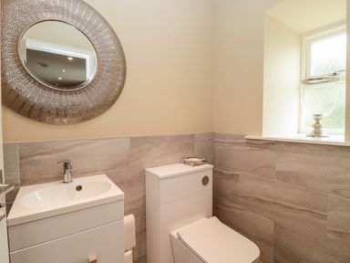 A bathroom with a sink and toilet and a round mirror above the sink at Calm Skies in Scremerston near Berwick-Upon-Tweed