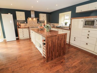 A kitchen with wooden floors and countertops a central island with shelves and wine rack and white cabinets at Calm Skies Scremerston near Berwick-Upon-Tweed