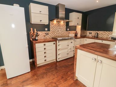 A kitchen with white cabinets wooden countertops a white refrigerator and a stove with a hood at Calm Skies Scremerston near Berwick-Upon-Tweed