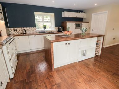 A kitchen with wooden floors white cabinets an island with fruit bowl and flowers at Calm Skies in Scremerston near Berwick-Upon-Tweed