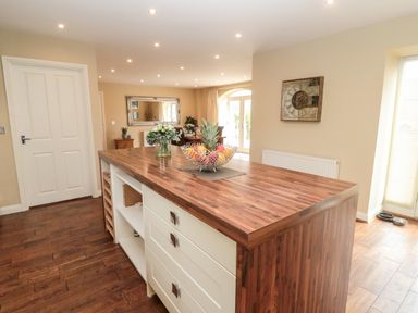 A kitchen island with a wooden countertop and drawers with fruit bowl and flowers in a vase at Calm Skies in Scremerston near Berwick-Upon-Tweed