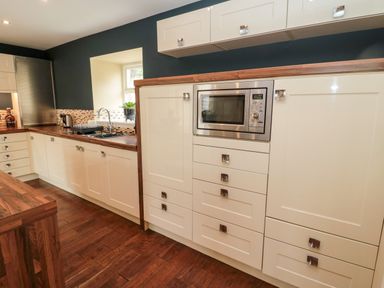 A kitchen with cream cabinets wooden countertops a microwave and a sink under a window at Calm Skies Scremerston near Berwick-Upon-Tweed