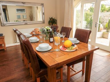 A dining room with a wooden table set for six with plates glasses and food near a glass door at Calm Skies Scremerston near Berwick-Upon-Tweed