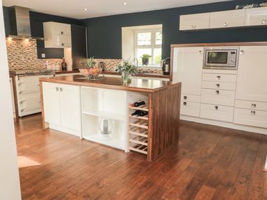 A kitchen with wooden floor, an island with wine rack, microwave, window, and cabinets at Calm Skies Scremerston near Berwick-Upon-Tweed