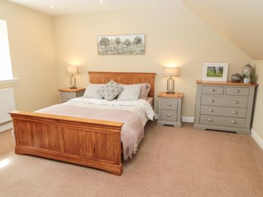 A bedroom with a wooden bed two bedside tables lamps and a dresser with decor at Calm Skies Scremerston near Berwick-Upon-Tweed