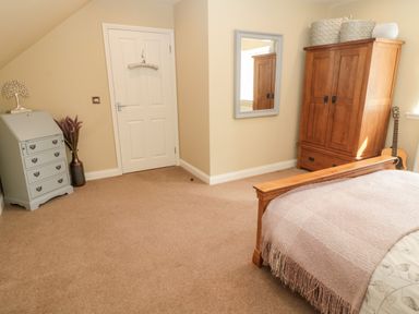 A bedroom with a wooden bed, wooden wardrobe, wall mirror, light blue chest of drawers, and a guitar at Calm Skies Scremerston near Berwick-Upon-Tweed