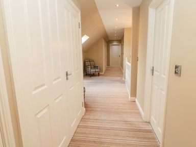 A hallway with striped carpet and white doors and a checkered armchair at Calm Skies Scremerston near Berwick-Upon-Tweed