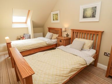 A bedroom with two wooden single beds a nightstand with a lamp and two framed pictures on the wall at Calm Skies Scremerston near Berwick-Upon-Tweed