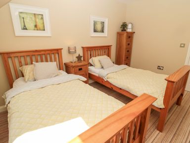 A bedroom with two single wooden beds bedside table and tall wooden chest at Calm Skies Scremerston near Berwick-Upon-Tweed
