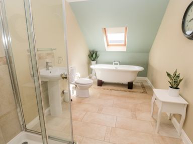 A bathroom with a shower, toilet, sink, freestanding bathtub, small table with a plant and a wall clock at Calm Skies in Scremerston near Berwick-Upon-Tweed