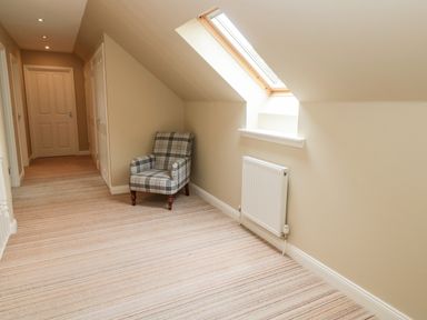 A hallway with a plaid armchair under a skylight window and a radiator on the wall at Calm Skies in Scremerston near Berwick-Upon-Tweed