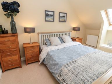 A bedroom with a double bed wooden bedside tables lamps a chest of drawers and a skylight window at Calm Skies Scremerston near Berwick-Upon-Tweed
