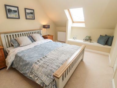 A bedroom with a double bed two nightstands a lamp and a window seat with cushions at Calm Skies Scremerston near Berwick-Upon-Tweed
