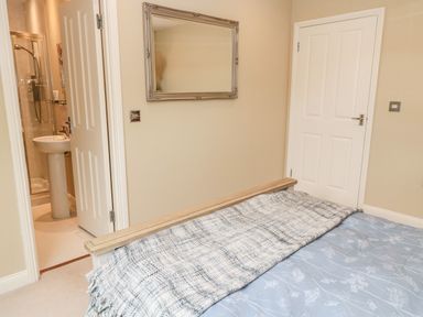 A bedroom with a bed and blanket a mirror on the wall and an open door showing a bathroom at Calm Skies Scremerston near Berwick-Upon-Tweed