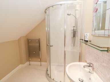 A bathroom with a curved glass shower enclosure a white sink with faucet a towel radiator and a mirror at Calm Skies Scremerston near Berwick-Upon-Tweed