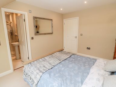 A bedroom with a bed covered with blue and white bedding a mirror on the wall a door leading to a bathroom and a closed door at Calm Skies Scremerston near Berwick-Upon-Tweed
