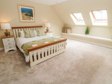 A bedroom with a bed a framed picture two bedside tables with lamps and windows on the slanted ceiling at Calm Skies Scremerston near Berwick-Upon-Tweed