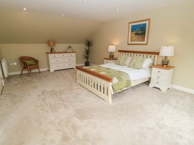 A bedroom with a bed nightstands lamps chair dresser and a plant at Calm Skies Scremerston near Berwick-Upon-Tweed