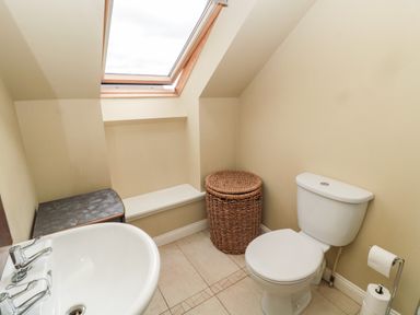 A bathroom with a toilet a sink a wicker laundry basket and a skylight window at Calm Skies in Scremerston near Berwick-Upon-Tweed