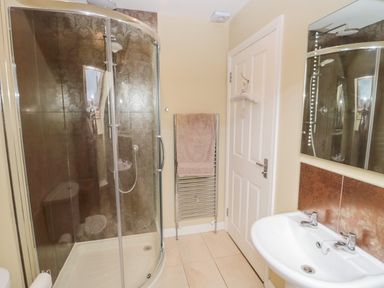 A bathroom with a corner shower cubicle a towel rack with a towel a white door and a sink with a mirror above at Calm Skies Scremerston near Berwick-Upon-Tweed