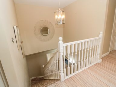 A stairway with white wooden railing and a striped carpet at Calm Skies Scremerston near Berwick-Upon-Tweed