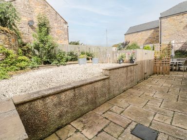 An outdoor patio area with stone paving gravel beds plants wooden fence and stone buildings at Calm Skies Scremerston near Berwick-Upon-Tweed