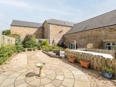 A stone patio with a bird bath surrounded by garden beds beside stone buildings at Calm Skies in Scremerston near Berwick-Upon-Tweed