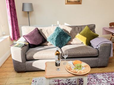 A living room with a beige sofa and colorful cushions a small wooden coffee table with wine and snacks at Healey Farm Cottage Rothbury