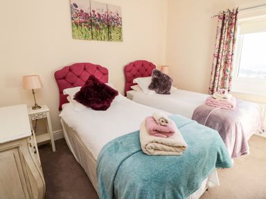 A bedroom with two single beds with pink headboards and folded towels by the window at Healey Farm Cottage in Rothbury