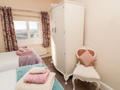 A bedroom with two beds towels on beds a white wardrobe a chair with a cushion and floral curtains at Healey Farm Cottage in Rothbury