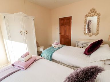A bedroom with two single beds a white wardrobe a chair a wooden door and a mirror at Healey Farm Cottage Rothbury
