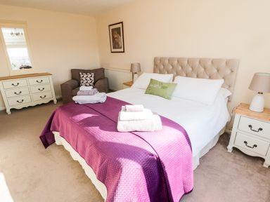 A bedroom with a bed covered in a purple blanket and white sheets with towels on top at Healey Farm Cottage in Rothbury
