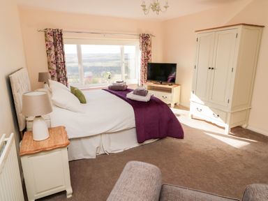 A bedroom with a bed, bedside table with lamp, wardrobe, TV on a stand, floral curtains and a window showing an outside view at Healey Farm Cottage in Rothbury