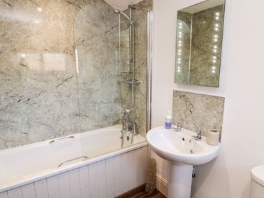A bathroom with a bathtub and shower combination a sink with a mirror above at Healey Farm Cottage in Rothbury
