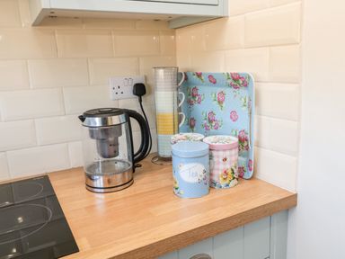 A kitchen countertop with an electric kettle mugs in a stand floral tins and a floral tray at Healey Farm Cottage in Rothbury