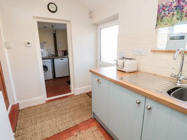 A kitchen with a sink toaster and wooden countertop with a door leading to a utility room with a washing machine and fridge at Healey Farm Cottage in Rothbury